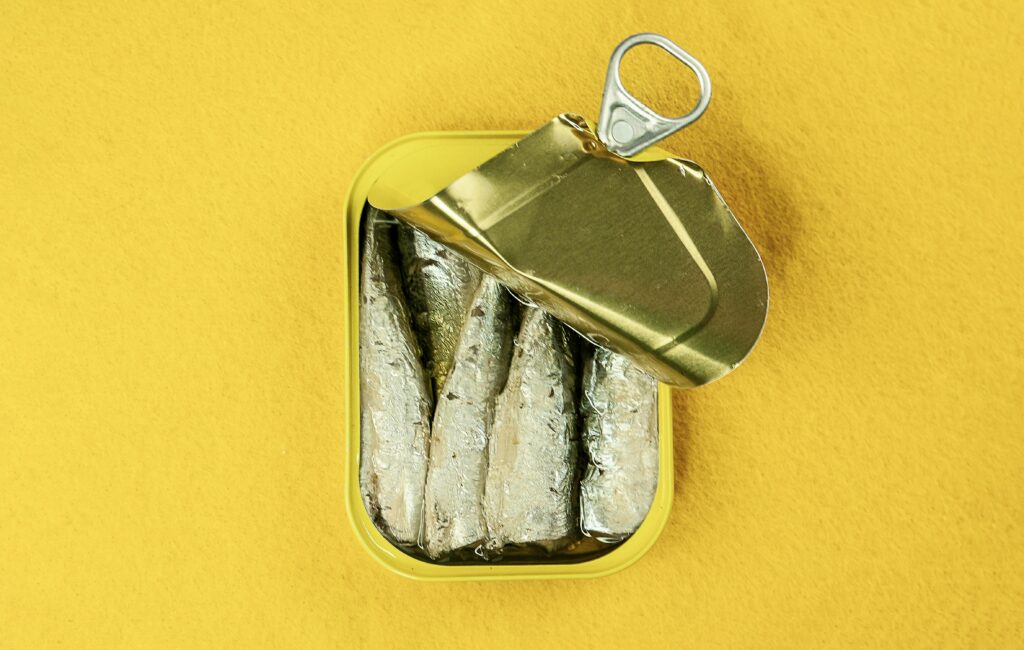 Open tin of sardines with lemon, showing small oily fish high in omega-3s and CoQ10