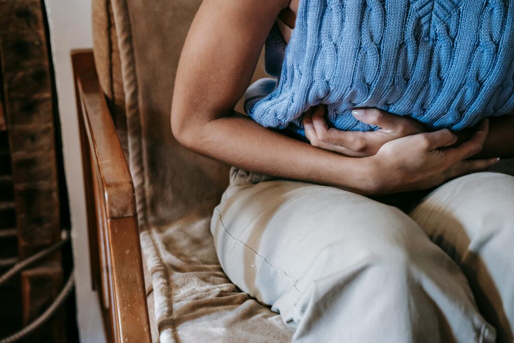 Woman sitting uncomfortably at a dining table holding her bloated stomach after eating, experiencing gut inflammation and leaky gut symptoms